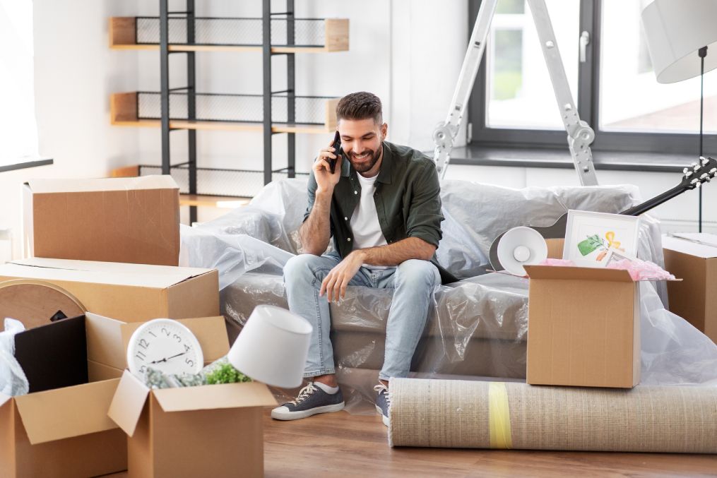 moving, people and real estate concept - happy smiling man with boxes calling on smartphone at new home