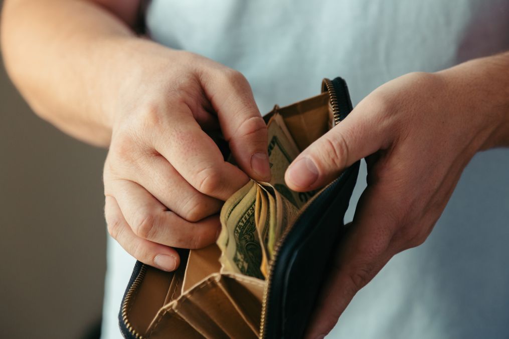 wallet with various dollar bills in the hands of a bankrupt man. Reduced costs, low salary