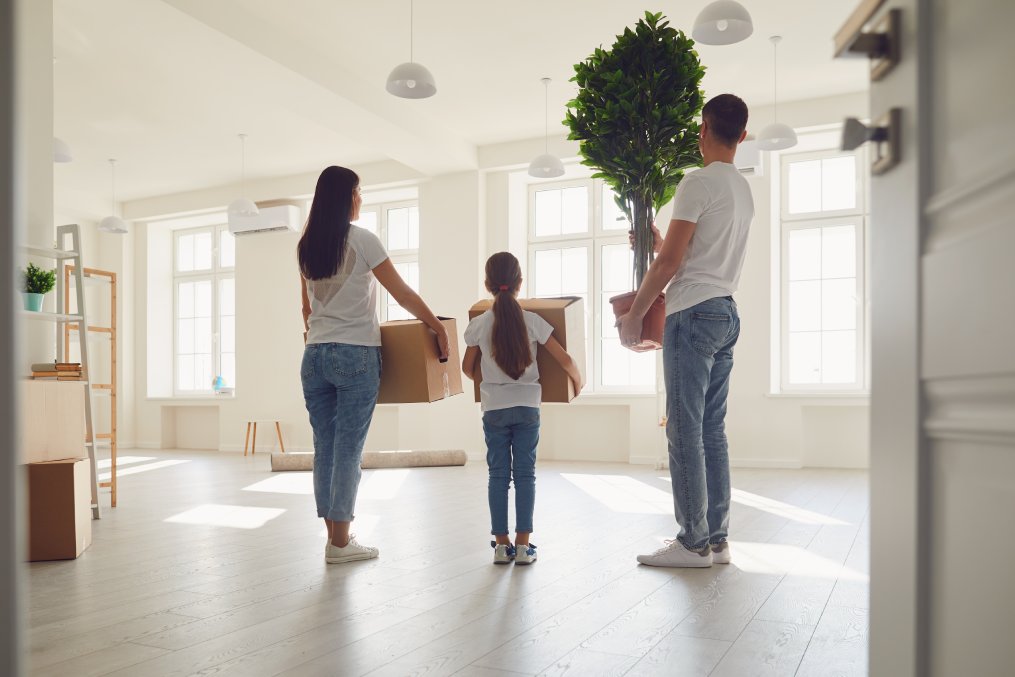 Happy family with children moving with boxes in a new apartment house. Back view.