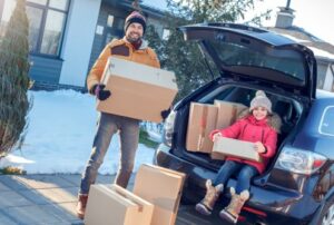 Fsther and daughter moving to new apartment together during winter standing outdoors near car taking boxes from trunk looking camera smiling excited