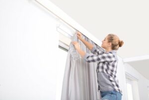 Woman hanging window curtain indoors. Interior decor element