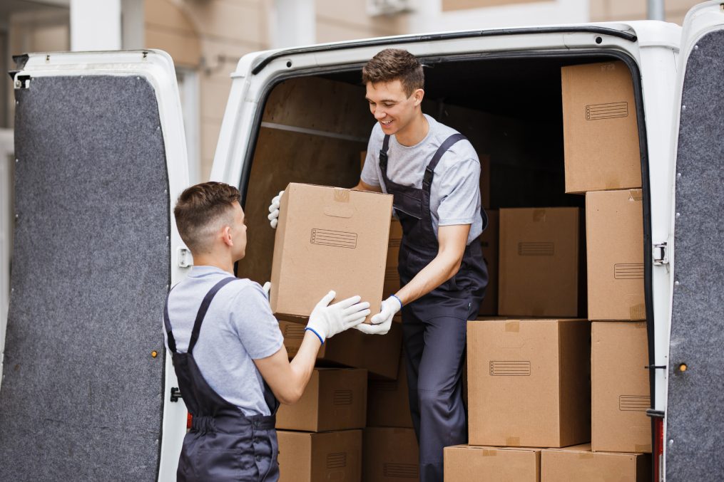 Two young handsome movers wearing uniforms are unloading the van