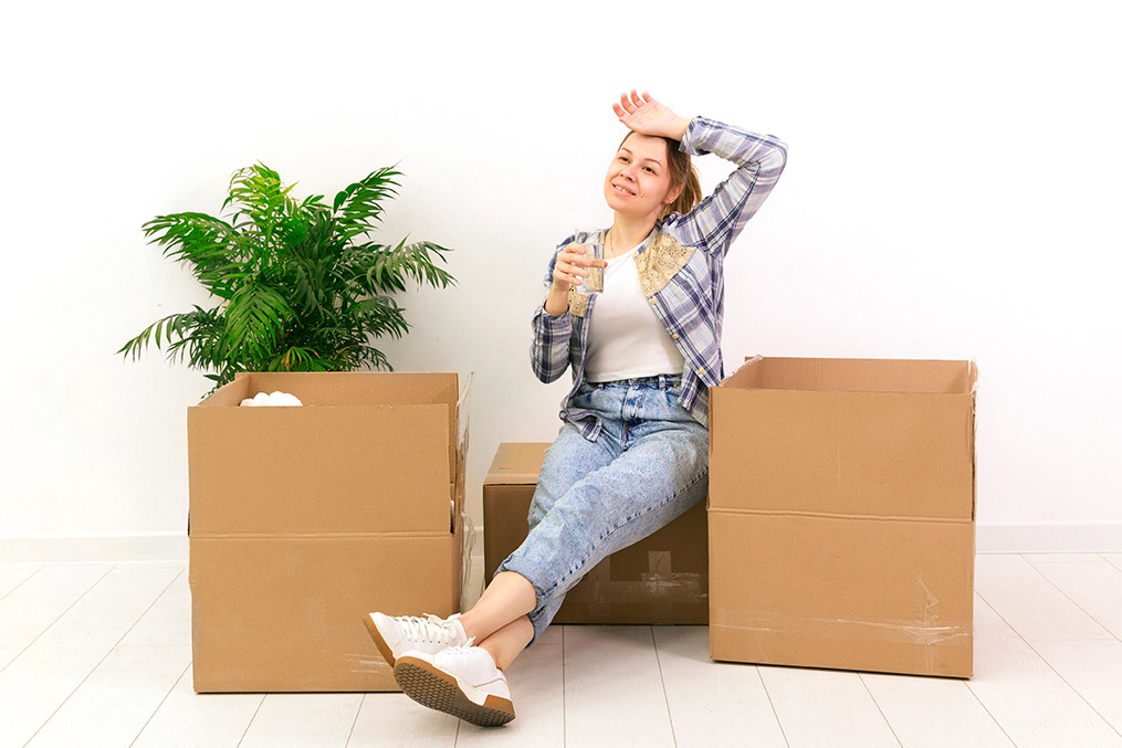 a woman resting over a moving box with her hands on her head, looking tired but happy