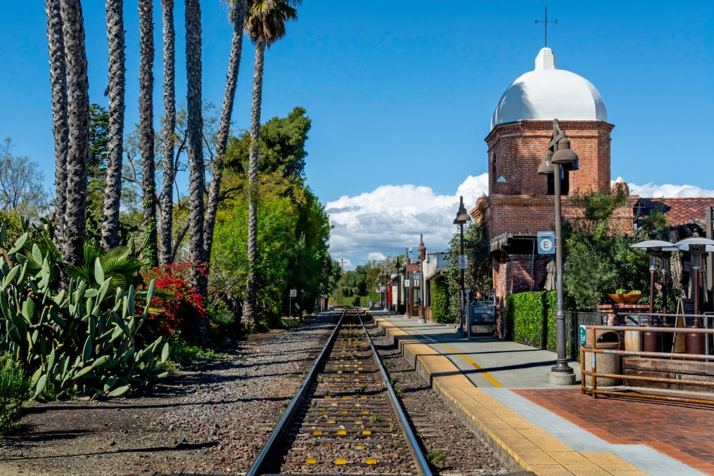 San Juan Capistrano, CA / USA - March 17, 2020: A single set of train tracks leads to a vanishing point on the horizon at a train station, whose architecture mimics a Catholic church.