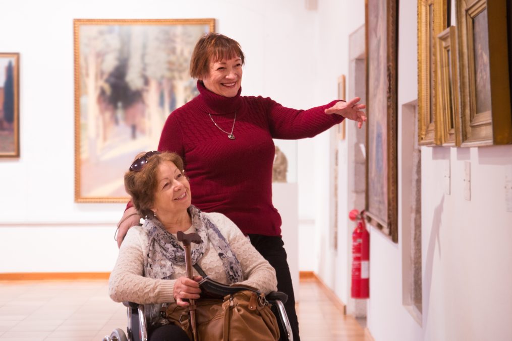 American woman and her handicapped female friend watching art works
