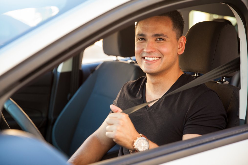 Portrait of a happy Hispanic young man putting his seatbelt on
