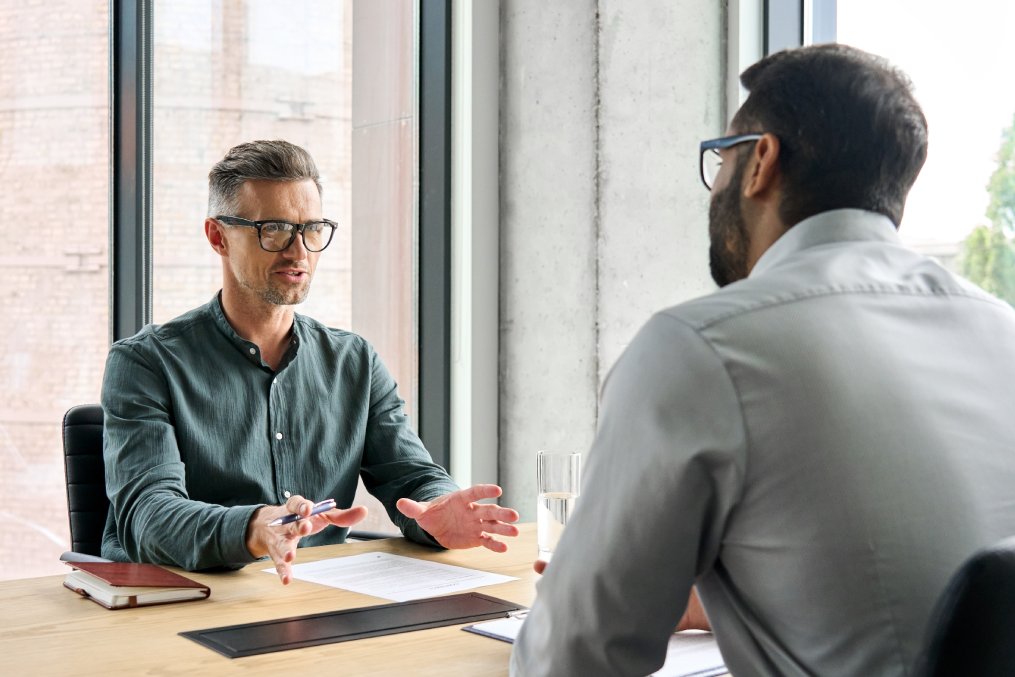 Two diverse business executive partners negotiating at board meeting, manager adviser consulting client discussing financial partnership contract sitting at table in office. Job interview concept.