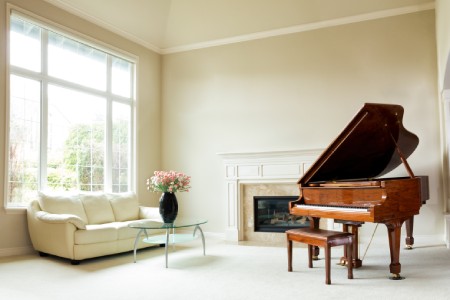 Living room with grand piano, fireplace, sofa and large window with bright daylight coming entering room.