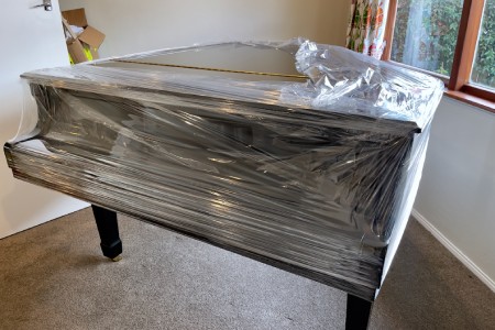 Glossy black grand piano partially covered in plastic wrap in preparation for removal by furniture moving company