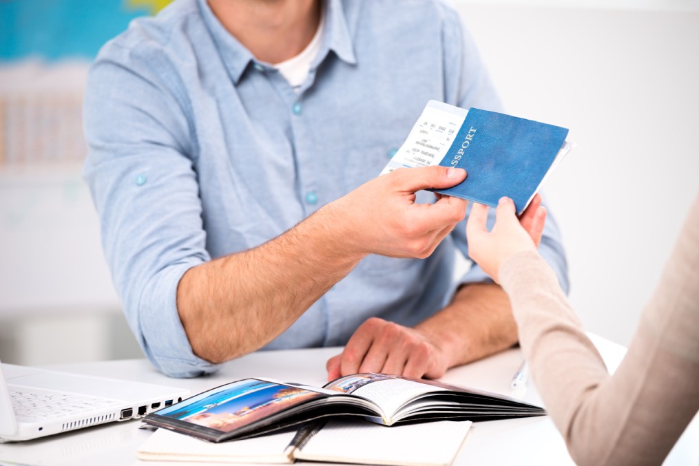 Close up photo of male travel agent and young woman. Young man giving tickets and passport with visa to female tourist