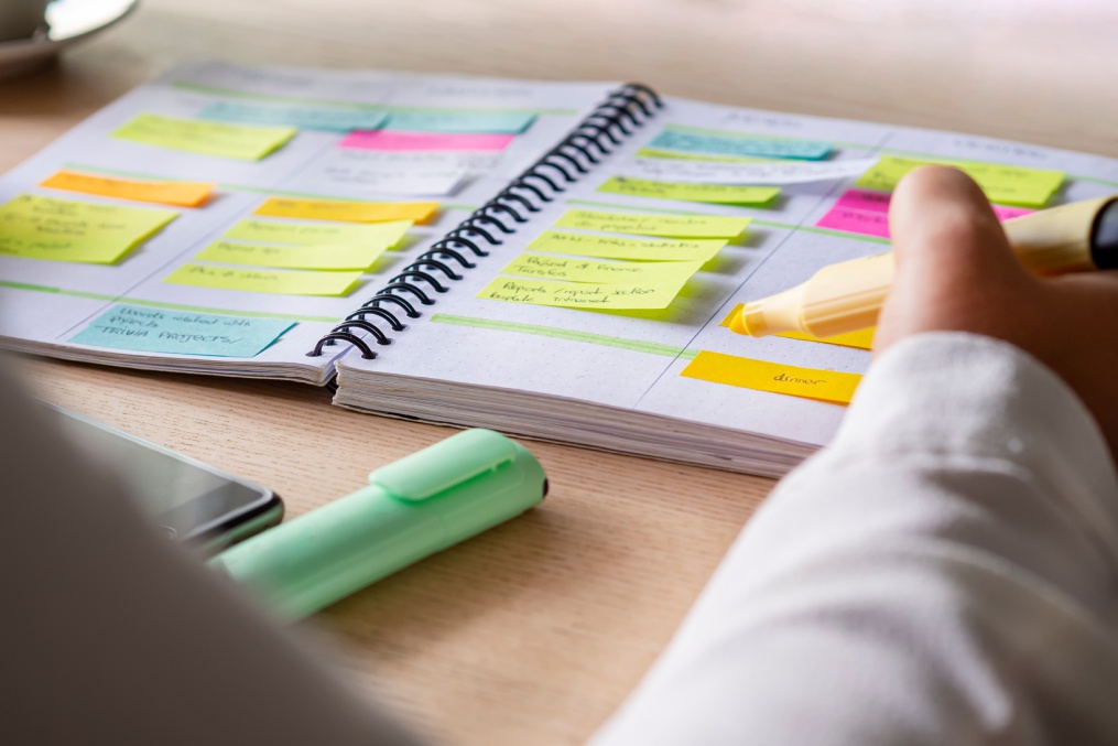 Close-up of agenda organize with color-coding sticky notes for time management. Productive schedule for appointments and reminders. Hand holding a yellow highlighter marker. Organization and planning