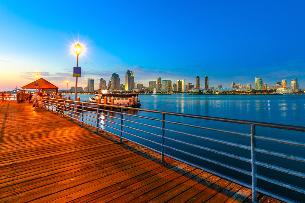 A scenic wooden pier leads to a waterfront, framed by the skyline of Coronado, CA, under a clear blue sky. Coer image: The Complete Guide to Moving to Coronado, CA