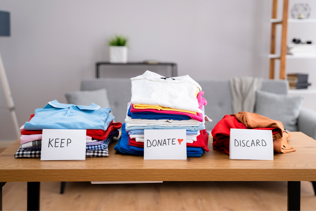 Clothes with separation for: donation, keep, discard. Cover image for Moving Sucks Less When You Declutter Before the Big Day