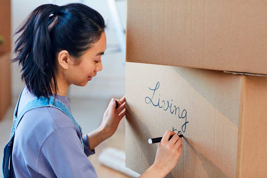 A woman writes "living room" on a moving box, illustrating the ease of decluttering during a move.