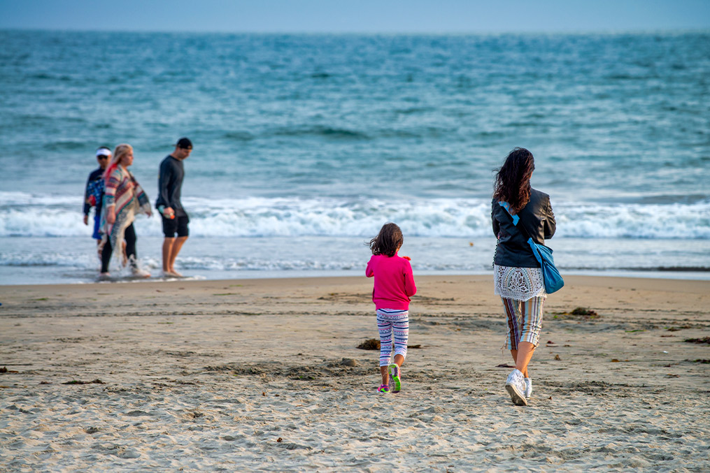 A family strolls on the beach, enjoying a sunny day while flying a vibrant kite in Coronado, CA.