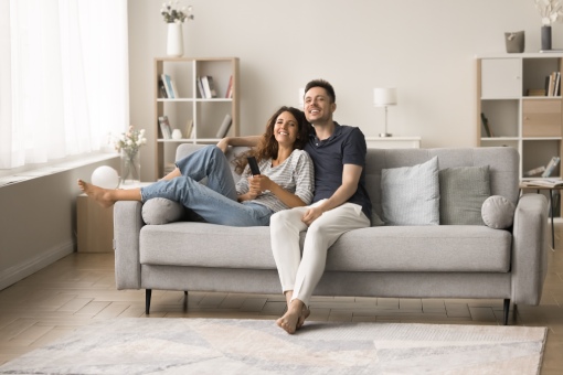 Cheerful millennial husband and wife in love relaxing on sofa together, hugging, watching TV show, sitcom series, movie, sport game broadcasting, laughing, enjoying leisure in modern home interior