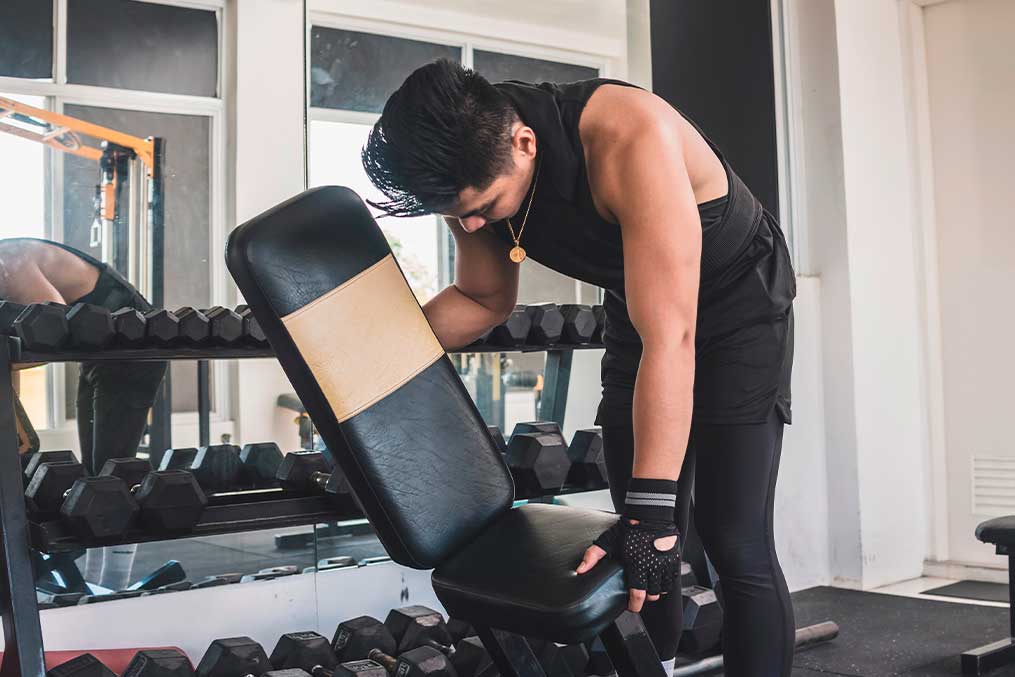 A man is seated on a gym bench, engaged in a workout, illustrating home gym equipment usage.