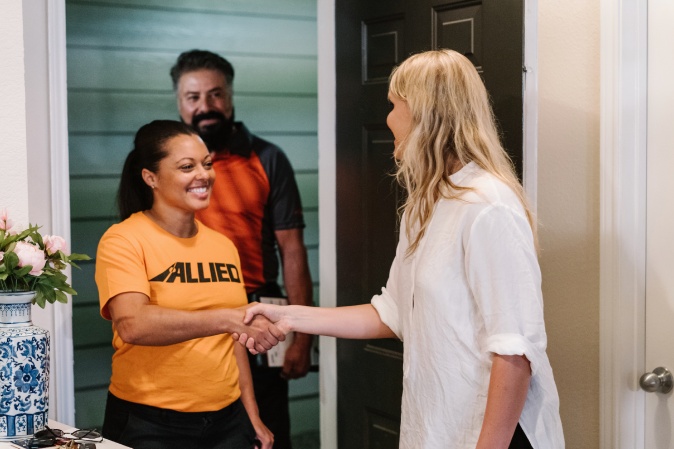 Allied moving team member greeting a customer with a handshake at the door, representing friendly and professional service for long-distance or cross-country moves