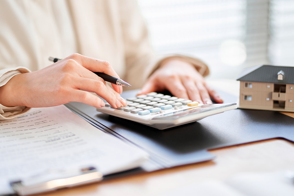 A woman's hand using a calculator, with a house model behind, illustrating the theme of relocating to Dubai from California.
