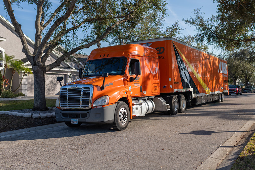  large orange moving truck driving down a street
