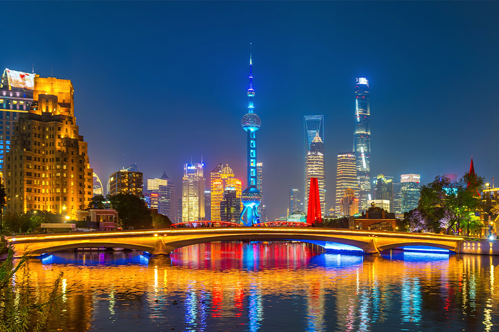 China: Nighttime city skyline glowing with lights, showcasing a bridge over water, representing a bustling urban landscape.