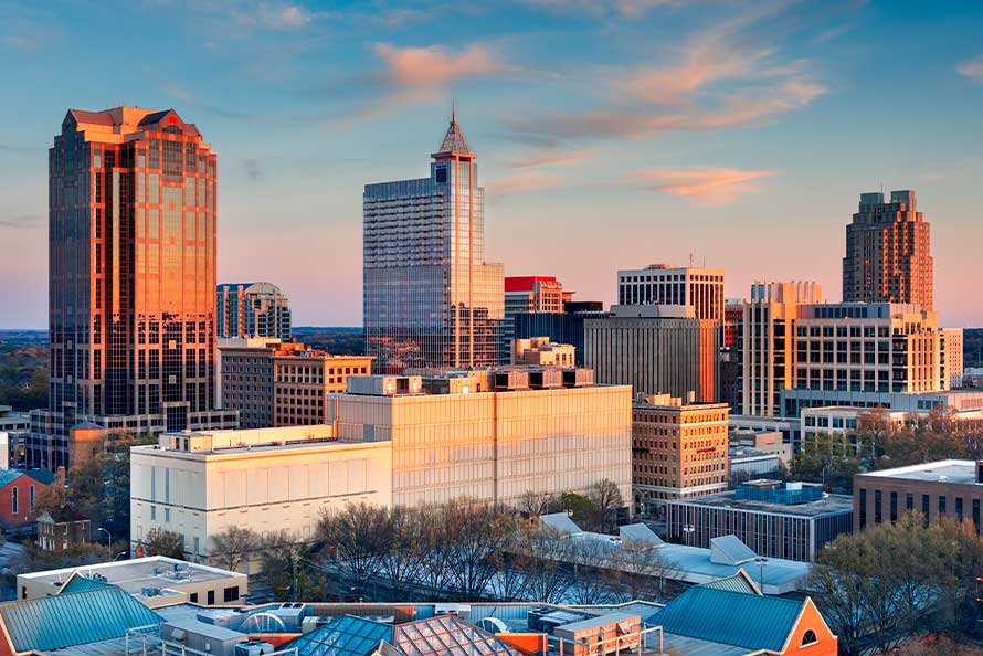 Sunset over Charlotte, NC, highlighting the city skyline with warm hues and the outlines of tall buildings.