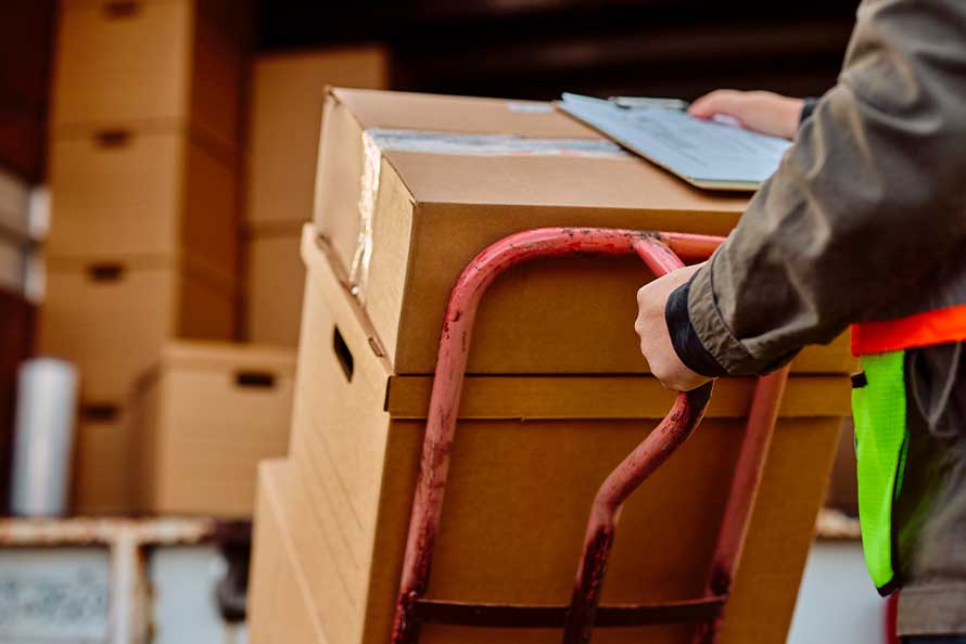 A man stands with a hand truck carrying a box, indicating a move from San Diego to Raleigh.