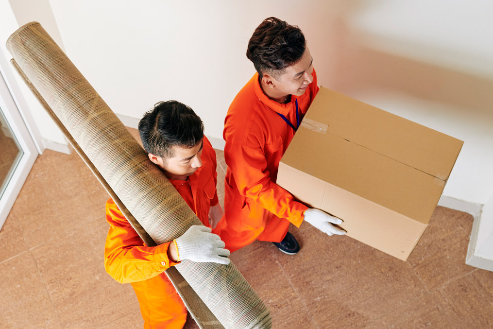 High angle view shot of two moving men wearing orange uniform carrying carpet and box with household things