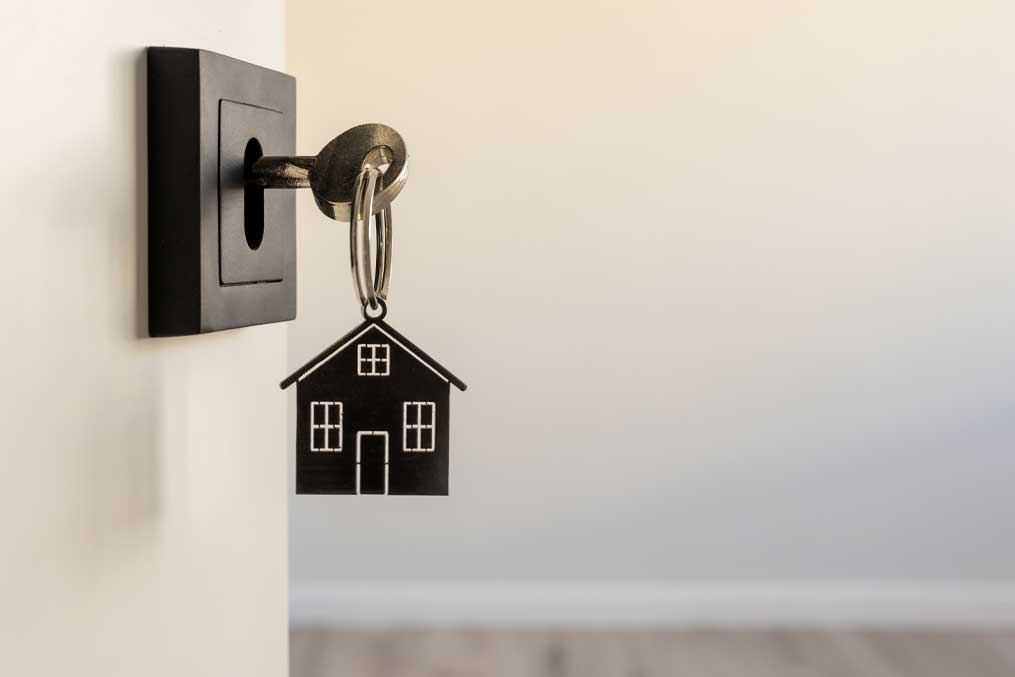 A key in a modern door lock with a house-shaped keychain, symbolizing real estate, homeownership, security, and new beginnings.
