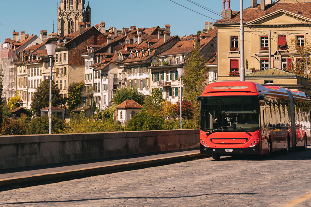 Red trolleybus traveling along a bridge with historic old town buildings and berner munster spire