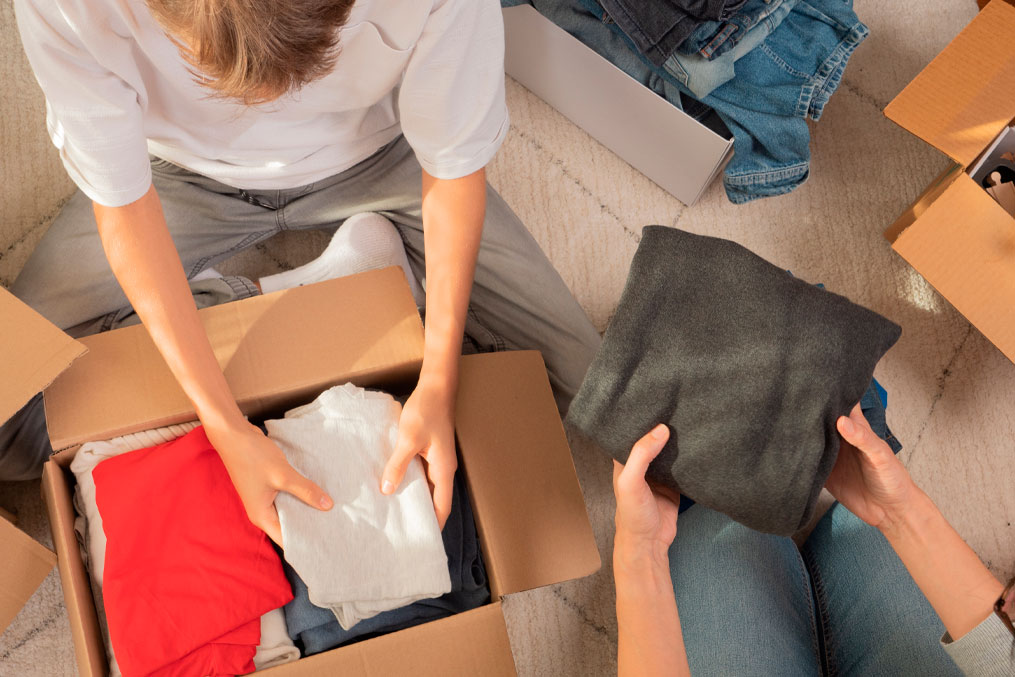 Woman and child sorting clothes and packing into cardboard box. Donations for charity, help low income families, declutter home, sell online, moving moving into new home, recycling, sustainable living