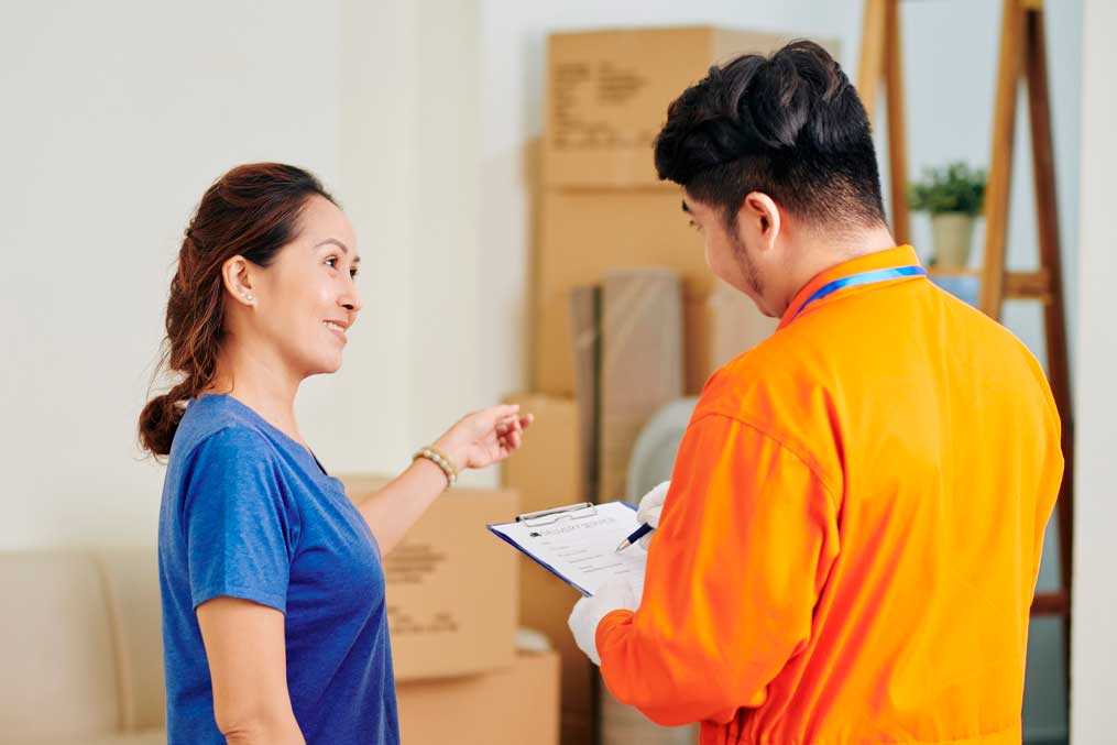 Horizontal medium shot of mature Asian woman asking questions to delivery service worker while he is making notes