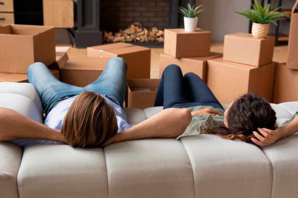 Let us have some rest. Young spouses relax on soft couch at modern luxury living room at moving day. Tired husband wife recline on sofa before unpacking things at rented flat enjoy new home. Rear view